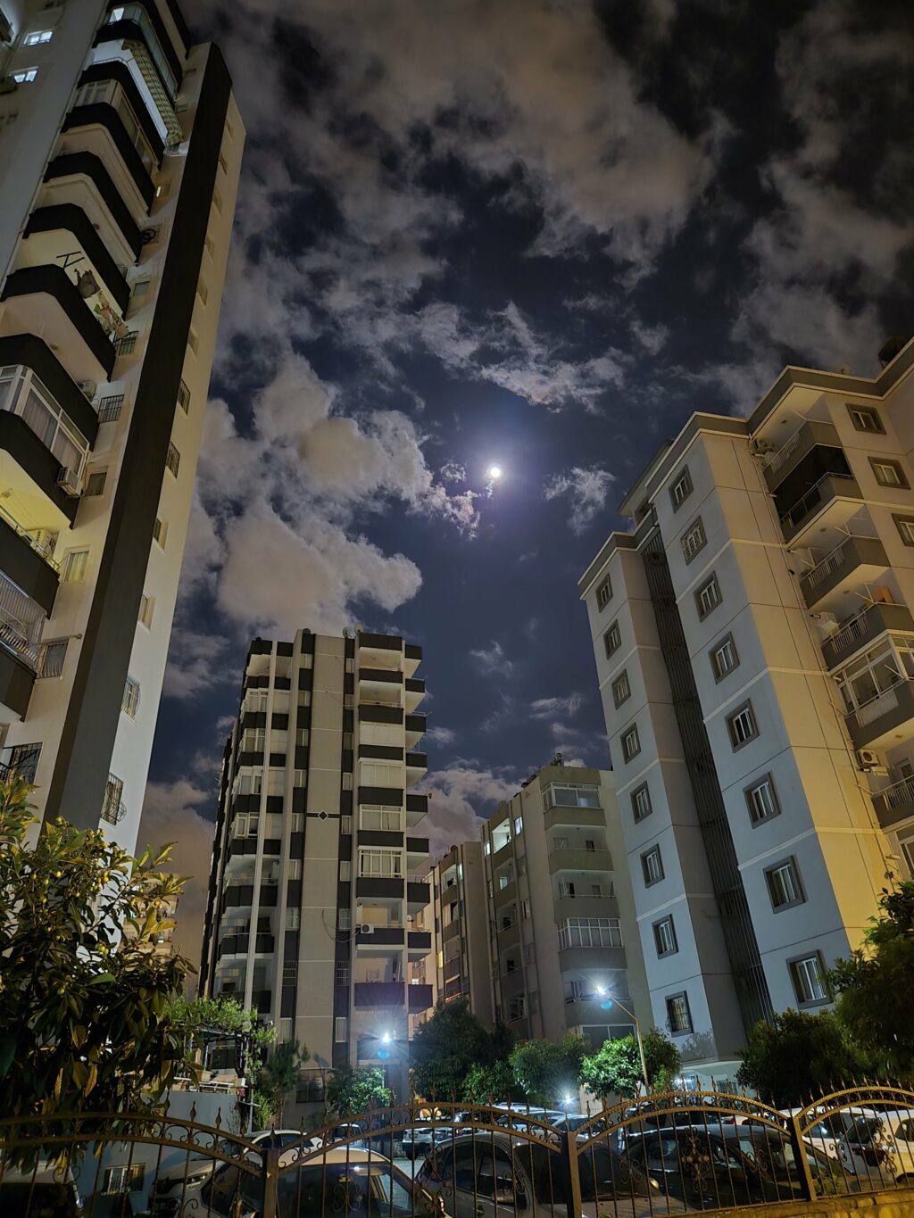 Gece çekimi, apartman binaları ve ay ışığıyla aydınlatılmış bir gökyüzü manzarası.