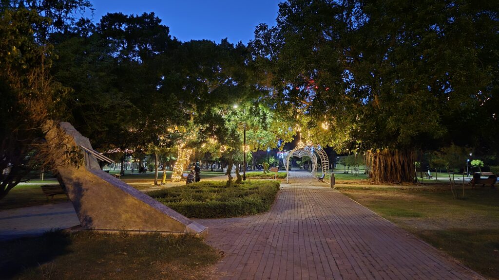Aydınlatılmış ağaçların ve yolların olduğu bir parkta, akşam saatlerinde çekilmiş gece manzarası.